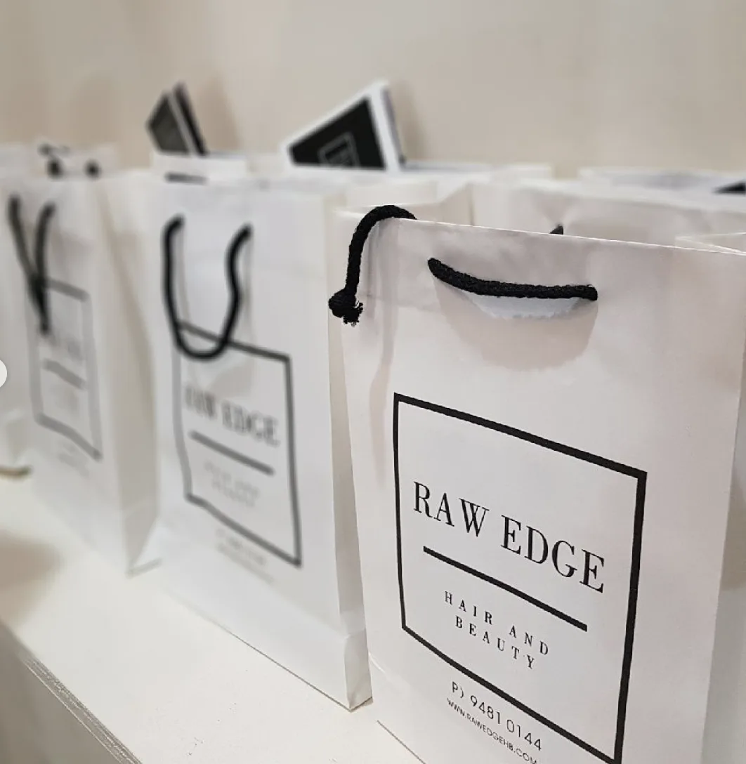 Row of Raw Edge branded white gift bags lined up in the salon